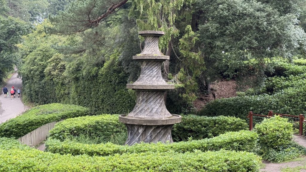 A monument with multiple tiers surrounded by small bushes.